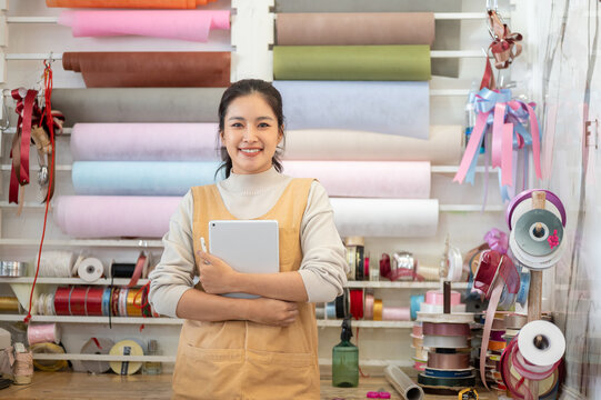 Retail woman worker holding tablet in colorful craft shop filled with wrap paper ribbon and supplies