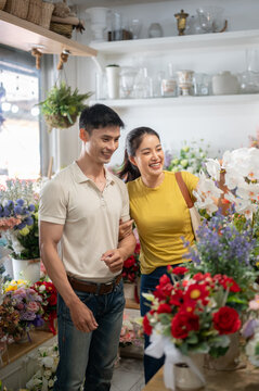 Asian couple man and woman linking arms walking together among beautiful displays inside flower shop