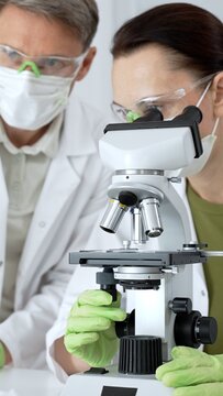 Expert medical researchers examining samples with a scientific microscope, collaborating on pharmaceutical development and biological discovery in a modern laboratory setting