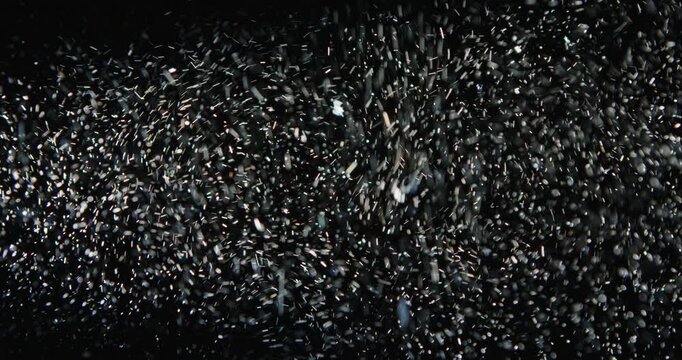 Tiny snow or dust randomly flying in the smoky air, empty space template for objects advertisement. Many dust particles cloud of white powder in low light on empty dark black contrast background.