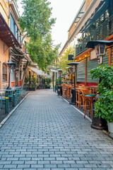 Fototapeta premium Pedestrian street with outdoor cafes, restaurant terraces, wooden tables, trees and traditional buildings in Athens, Greece. Urban tourism, Mediterranean hospitality, walkable city