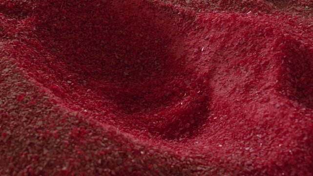 heaped mass of crimson shredded flakes fills the frame, coarse and uneven with pale specks scattered through, lit from above