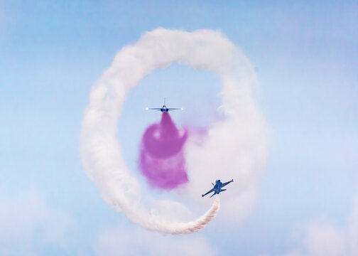 Aerial view of Korea Black Eagles fighter jets performing a synchronized aerial maneuver with white and purple smoke trails against a clear blue sky at the Changi Exhibition Centre, Singapore.