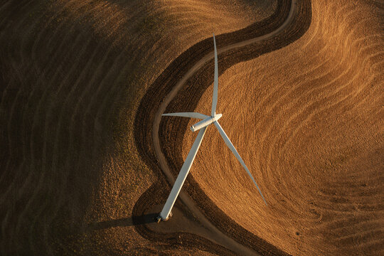 Aerial view of a wind turbine standing in a golden field with textured soil patterns in Rio Vista, California, United States.