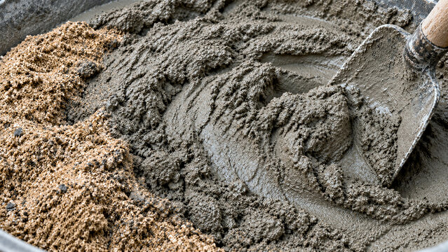 Shovel mixing wet cement mortar with sand in a container. Close-up of construction material preparation with tools. Building, renovation and masonry work concept.