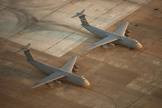 Aerial view of two C-5 Galaxy military transport aircraft parked on the tarmac at Travis Air Force Base during golden hour in Fairfield, California, United States.