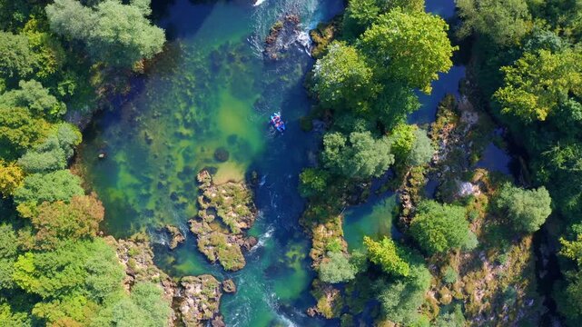 Aerial view of people rafting on clear turquoise Una river surrounded by green forest in Bosnia and Herzegovina
