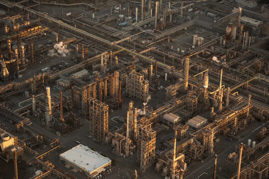 Aerial view of the Chevron Richmond Refinery with industrial pipes, towers, and storage tanks illuminated by golden hour light in Richmond, California, United States.