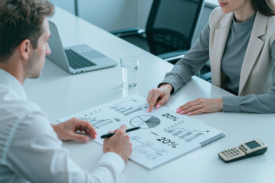 Caucasian businesswoman and businessman reviewing financial charts, discussing performance metrics and budget planning in office. Ideal for corporate strategy, analytics, consulting