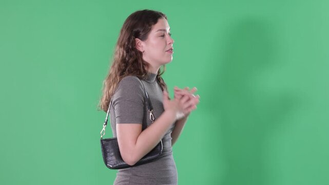Young woman stands in front of green screen talking or recording talking video 