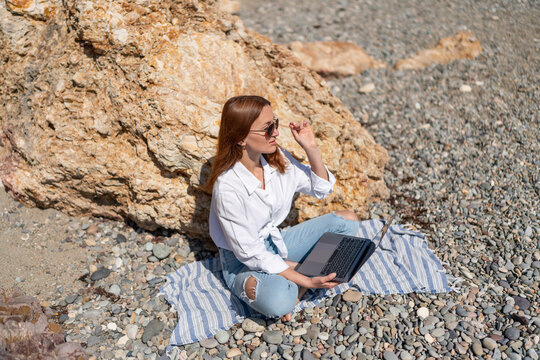 Remote work lifestyle for woman sitting on seaside rock with laptop