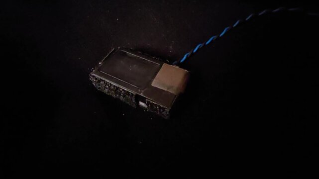 High Angle Macro Shot of a Disassembled Projector DMD Chip Module and Optical Display Sensor Component with Twisted Connecting Wires on Dark Background