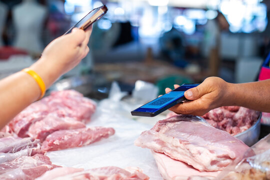 Selective focus to customer using a smartphone to make a contactless simulate QR code payment to a vendor at a fresh meat market stall. Modern cashless transaction concept.