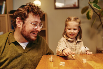 Naklejka premium Caucasian father and kid daughter playing dreidel game during Hanukkah celebration. Image suitable for cultural heritage, family lifestyle, and holiday marketing