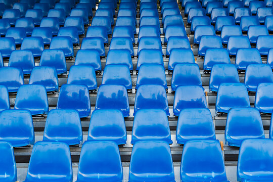 Rows of empty blue plastic seats in stadium, repeated seating pattern in sports arena grandstand, outdoor tribune background, nobody, daytime