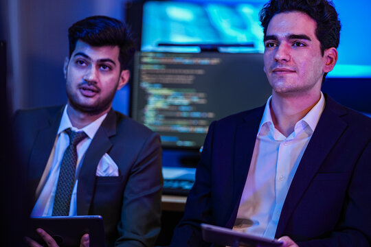 Two colleagues react to the same point at once as the session runs into the evening inside a dark modern technology office during a focused late-night working session