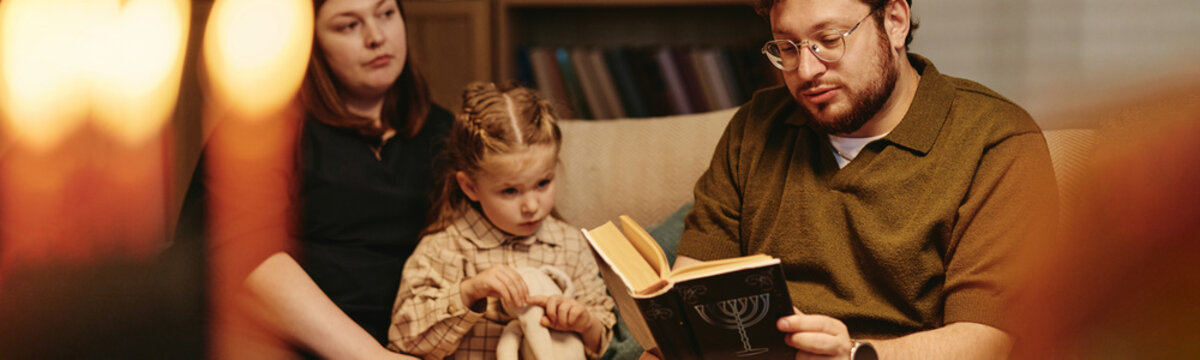 Jewish Caucasian family with young adult parents and female child reading book together at home. Image suitable for cultural education, religious holiday advertising, lifestyle marketing