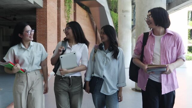 Close knit group male and female Asian students walk row inside university building greeting each friendly smiles cheerful expressions carrying backpacks textbooks and laptops ready afternoon classes.