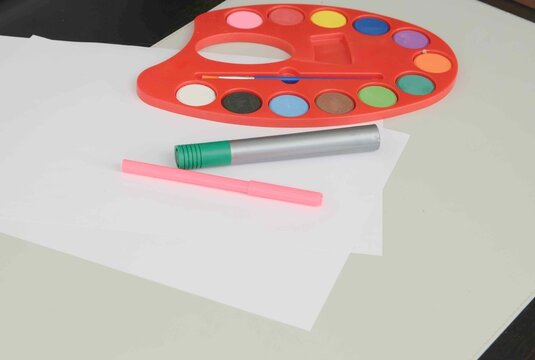 Colorful art supplies on a table with paint palette, brush, and paper for creative projects at a workspace