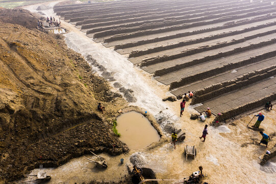 Aerial view of the brick fields with rows of drying bricks, workers moving across the muddy ground, and wheelbarrows in Aminbazar, Dhaka Division, Bangladesh.