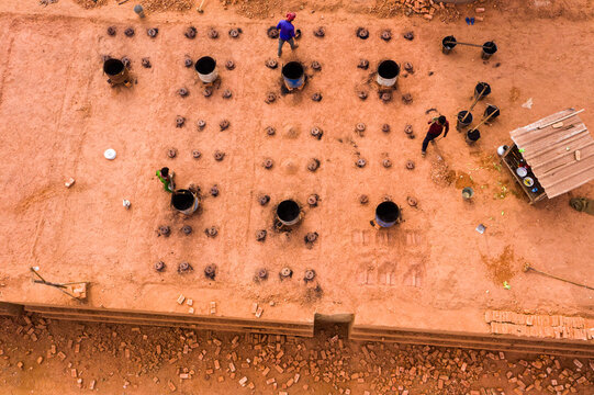 Aerial view of workers operating a brick kiln with rows of barrels on red soil in Aminbazar, Dhaka Division, Bangladesh.