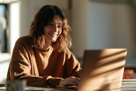 Joyful woman smiles while using a laptop in a bright home office setting