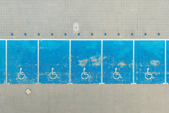 Aerial view of blue-painted accessible parking spaces with white wheelchair symbols on the pavement in Poland.