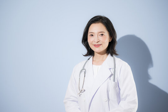 [水色背景]聴診器をつけて白衣を着る女性医師、笑顔でカメラ目線日本人ドクターのポートレート