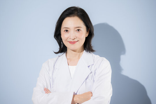 [水色背景]白衣を着て考える腕を組むポーズをする女性医師、笑顔でカメラ目線日本人ドクターのポートレート