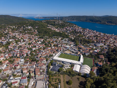 Aerial view of the Yusuf Ziya Onis Stadium surrounded by dense residential buildings, green hills, and the Bosphorus in Sariyer, Istanbul, Turkey.