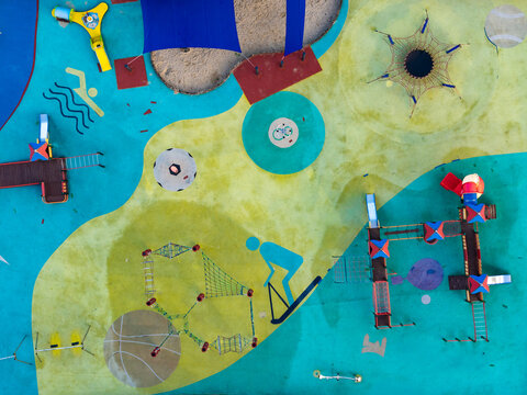 Aerial view of a colorful playground with various play structures, climbing nets, slides, and painted graphics on the rubber flooring in Poland.