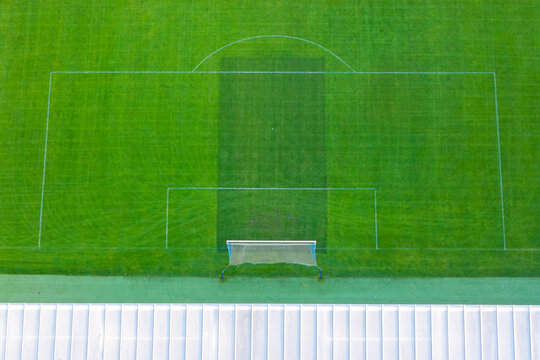 Aerial view of a modern football field with white pitch markings and a goal net, set against a green grass surface in Poland.