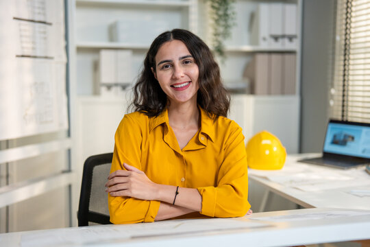 Portrait of Hispanic woman architect sitting at desk, working in office.