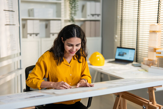 Young Hispanic woman architect sitting at her desk working in an office. 