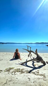 Young woman sitting on the sand at the water's edge on an idyllic beach.