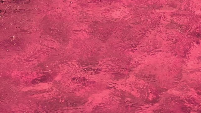 Red-tinted water surface displaying dynamic ripples and fluid movement. Organic patterns create a visually engaging and richly textured background with varying shades of red, enhancing depth and.
