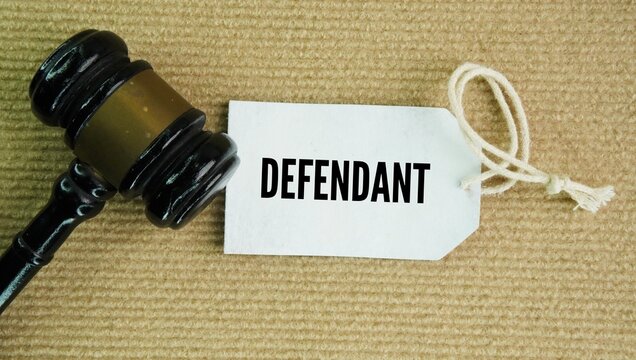 Judge's gavel and paper tag with the words defendant is a person or group accused of a crime or sued in a court of law.