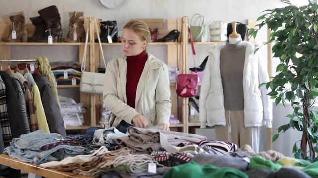 While shopping, teen girl browsing goods items and choose elect denim jeans in store, buyer consider some items. Concept of seasonal wardrobe shopping. Client and holiday shopping. 