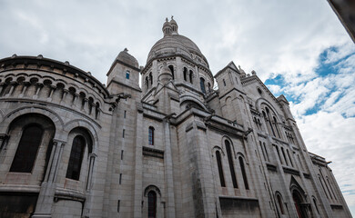 Fototapeta premium Sacré-cœur basilica architecture against a cloudy sky, looking up at the iconic montmartre landmark in paris