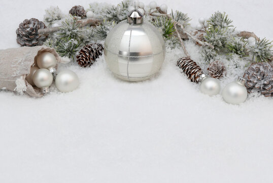 Christmas background featuring white snow, space for text, silver Christmas ornaments, and wintry fir branches.