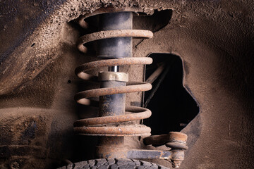 Rusty car front strut assembly with coil spring and shock absorber inside dirty wheel well © Yevhenii
