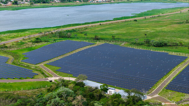 Aerial view of a large solar farm with rows of photovoltaic panels situated in green fields near a river in Posadas, Misiones Province, Argentina.