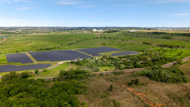 Aerial view of a large solar farm featuring rows of photovoltaic panels set within a green landscape with trees and a road in Posadas, Misiones Province, Argentina.