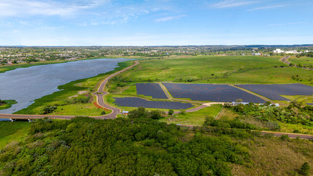 Aerial view of a large solar farm installation situated near a river and lush green fields in Posadas, Misiones Province, Argentina.