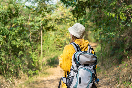 Rear view of female hiker with backpack walking on trail in mountains.