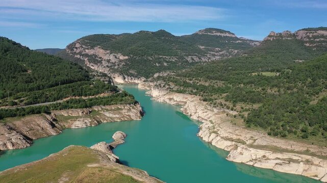 Turquoise Llosa del Cavall Reservoir on Cardener River winding through picturesque mountainous landscape in Catalonia, Spain, surrounded by lush greenery and rocky cliffs under clear blue sky