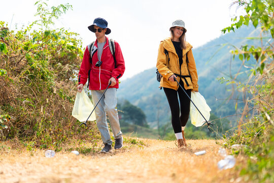 Two hikers collecting trash while walking along a mountain trail.