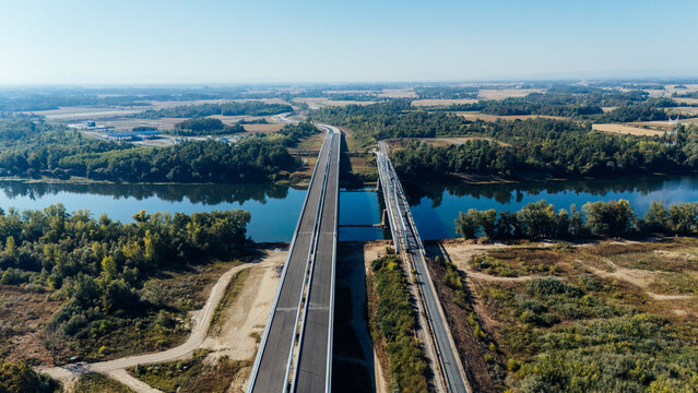 Aerial view of the Racha Bridge spanning the Sava River, surrounded by lush green forests and rural landscape under a clear blue sky in Sremska Raca, Vojvodina, Serbia.