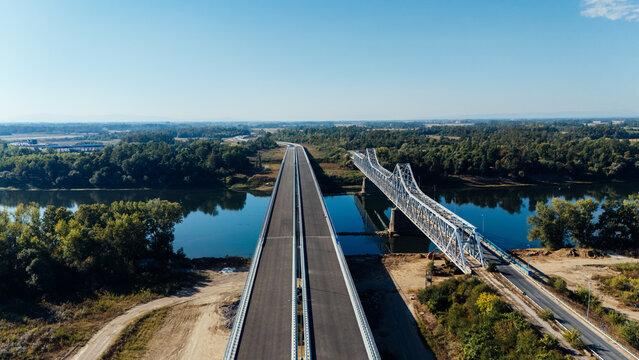 Aerial view of Racha Bridge spanning the Sava River with a new highway bridge under construction, surrounded by lush green forests under a clear blue sky Sremska Raca, Vojvodina, Serbia.