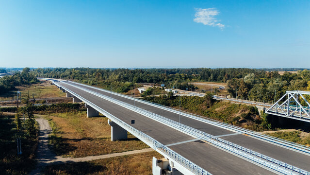 Aerial view of Racha Bridge spanning the landscape with modern road infrastructure surrounded by lush trees under a clear blue sky in Sremska Raca, Vojvodina, Serbia.